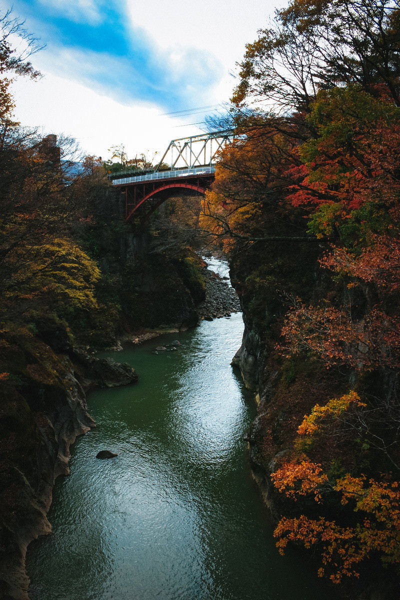吾妻渓谷の川に架かる鉄橋と周囲の秋の紅葉が映る風景