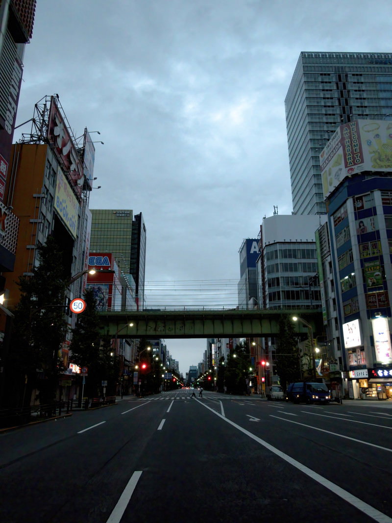 早朝の薄明かりの中、高層ビルが立ち並ぶ秋葉原の街並みと車道上の高架橋
