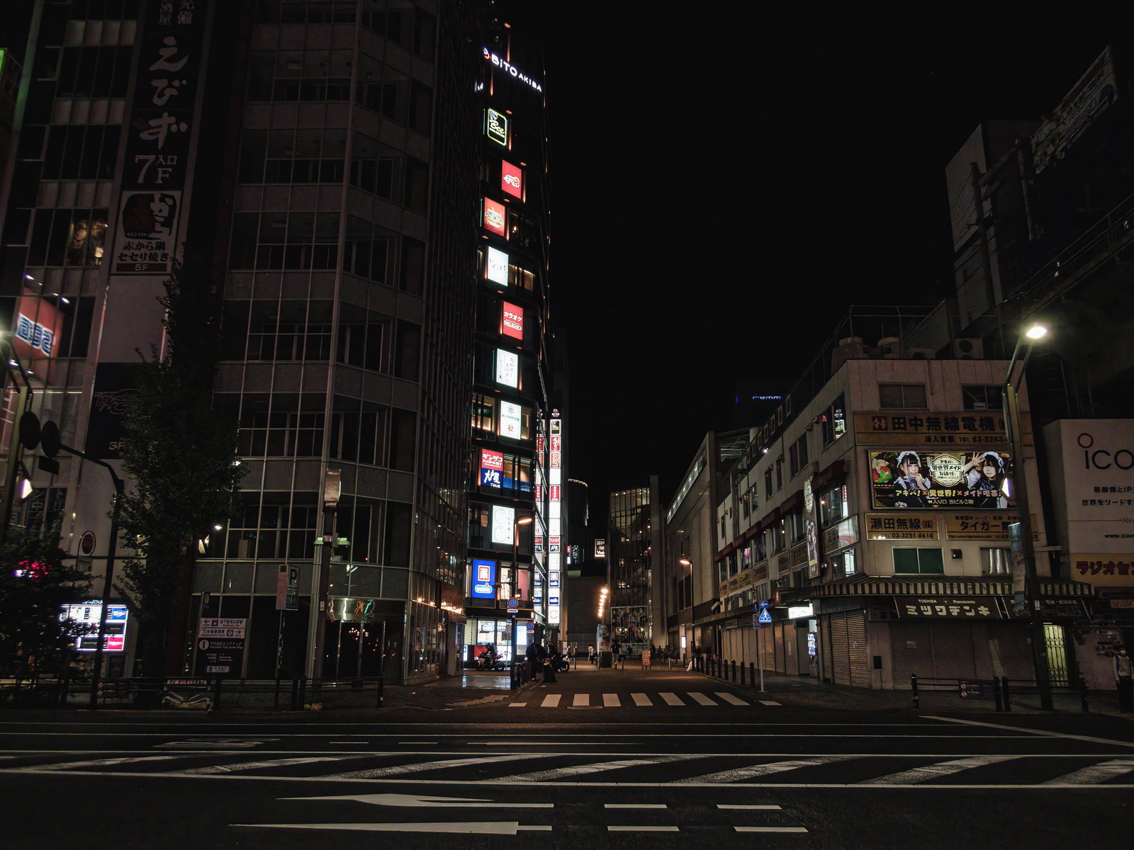 夜の秋葉原の路地に立つ赤い照明の袖看板とビル街