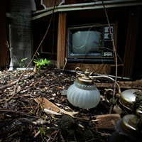 剥き出しの地面に落ちたアンティークの照明器具とテレビの写真