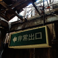 廃モーテルの天井から錆びたチェーンで吊るされた緑色の非常出口看板の写真