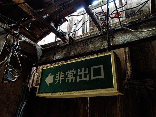 廃モーテルの天井から錆びたチェーンで吊るされた緑色の非常出口看板
