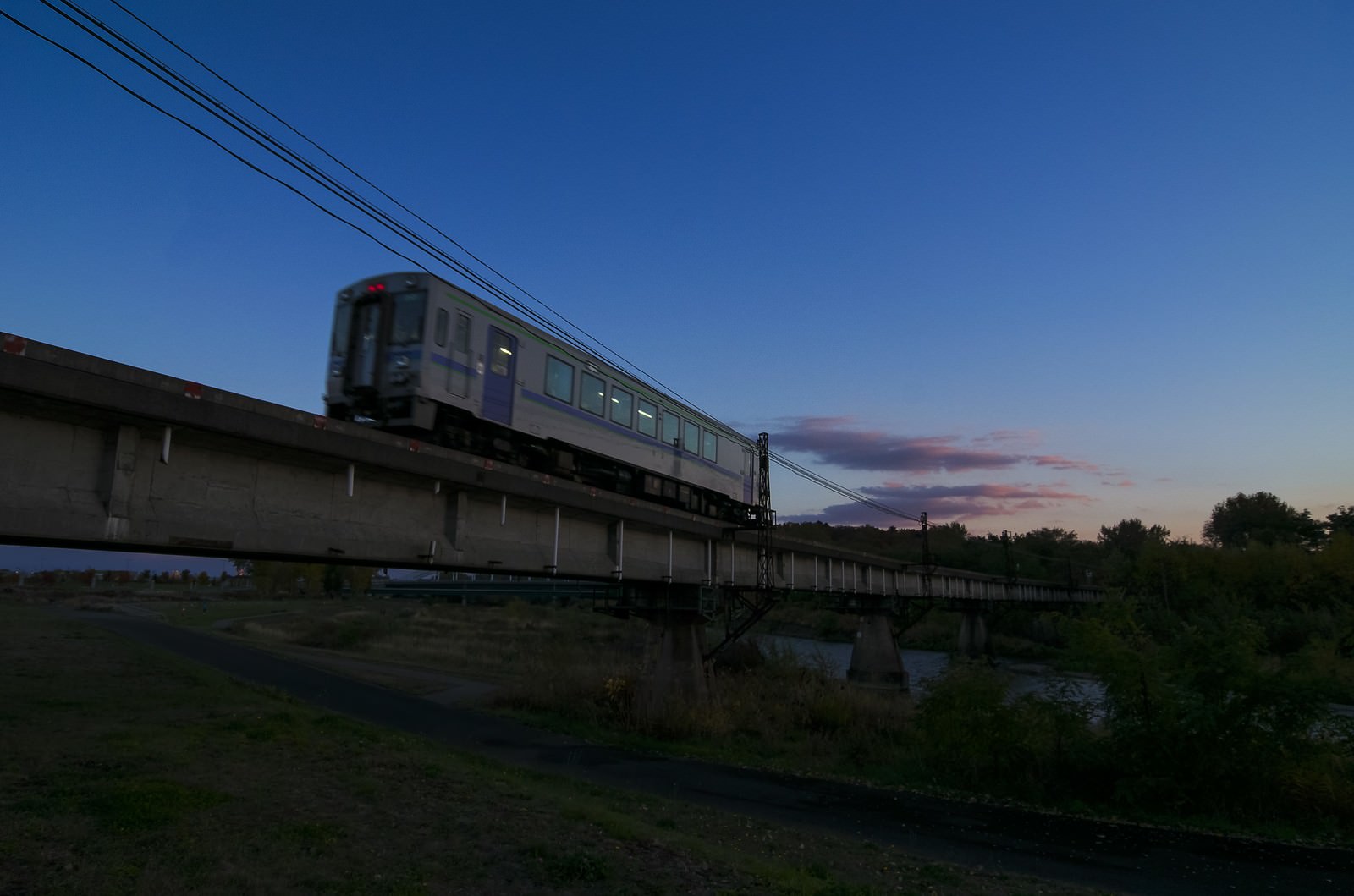 旭川のローカル線が夕暮れの橋を走行する風景