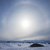 雪原と山並みの上空に浮かぶ日輪のハロ現象の写真