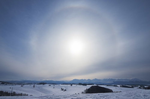 雪原と山並みの上空に浮かぶ日輪のハロ現象