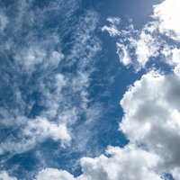 白い雲が浮かぶ昼の太陽が照りつける青い空の写真