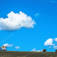 青空とトラクターと牧草ロールの北海道風景の写真