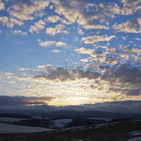 雪の残る畑と夕焼け空に染まる山並みの写真