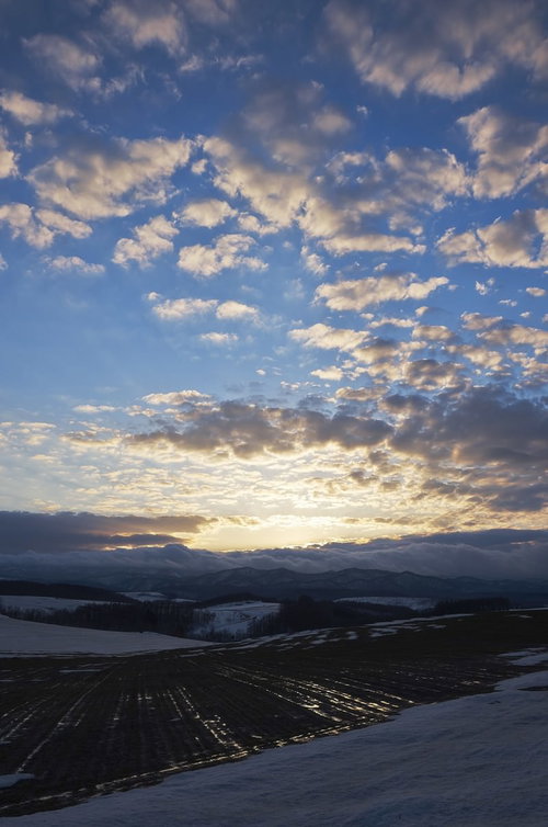 雪の残る畑と夕焼け空に染まる山並み