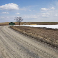 雪解けの畑と緑の小屋が建つ田舎の砂利道の写真