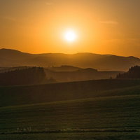 夕暮れのオレンジの光に包まれる美瑛の丘のシルエットの写真