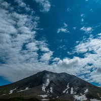 噴煙が上がる旭岳の山肌と青空の写真