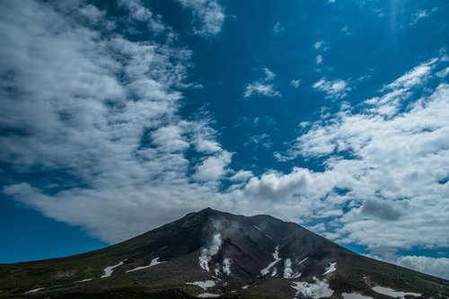 噴煙が上がる旭岳の山肌と青空