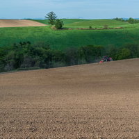 緑のパッチワーク畑が広がる美瑛の丘で耕す農家の写真