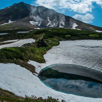 雪が残る旭岳と青い火口湖の写真