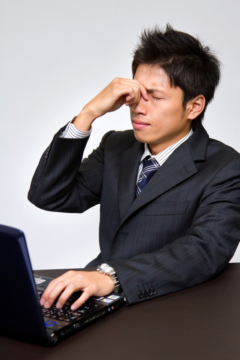 PCの前で目の疲れに鼻を押さえる男性［モデル：恭平］