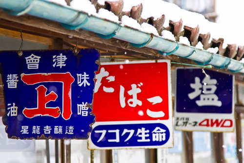 青い瓦屋根に雪が積もった田舎の商店と日本語看板