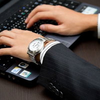 木目の机でノートパソコンのキーボードに手を置くビジネスマンの写真