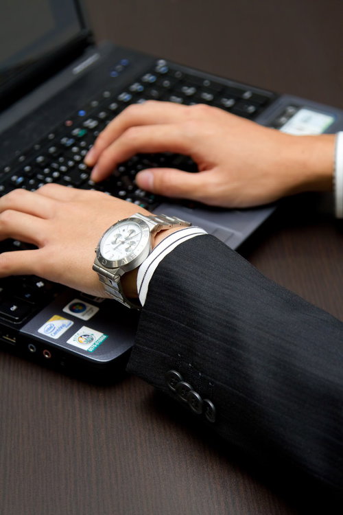 木目の机でノートパソコンのキーボードに手を置くビジネスマン