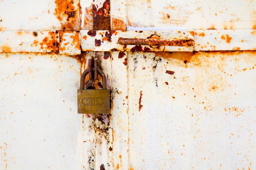SOLの刻印がある錆びた白い鉄扉に掛かる南京錠