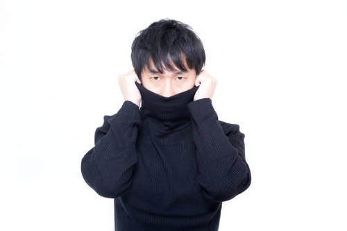 黒いタートルネックの襟を両手で持ち上げるスタジオの人物