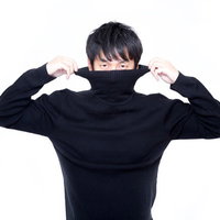 黒いタートルネックの襟を両手で引き上げる短髪男性の写真