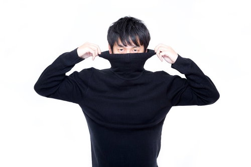 黒いタートルネックの襟を両手で引き上げる短髪男性