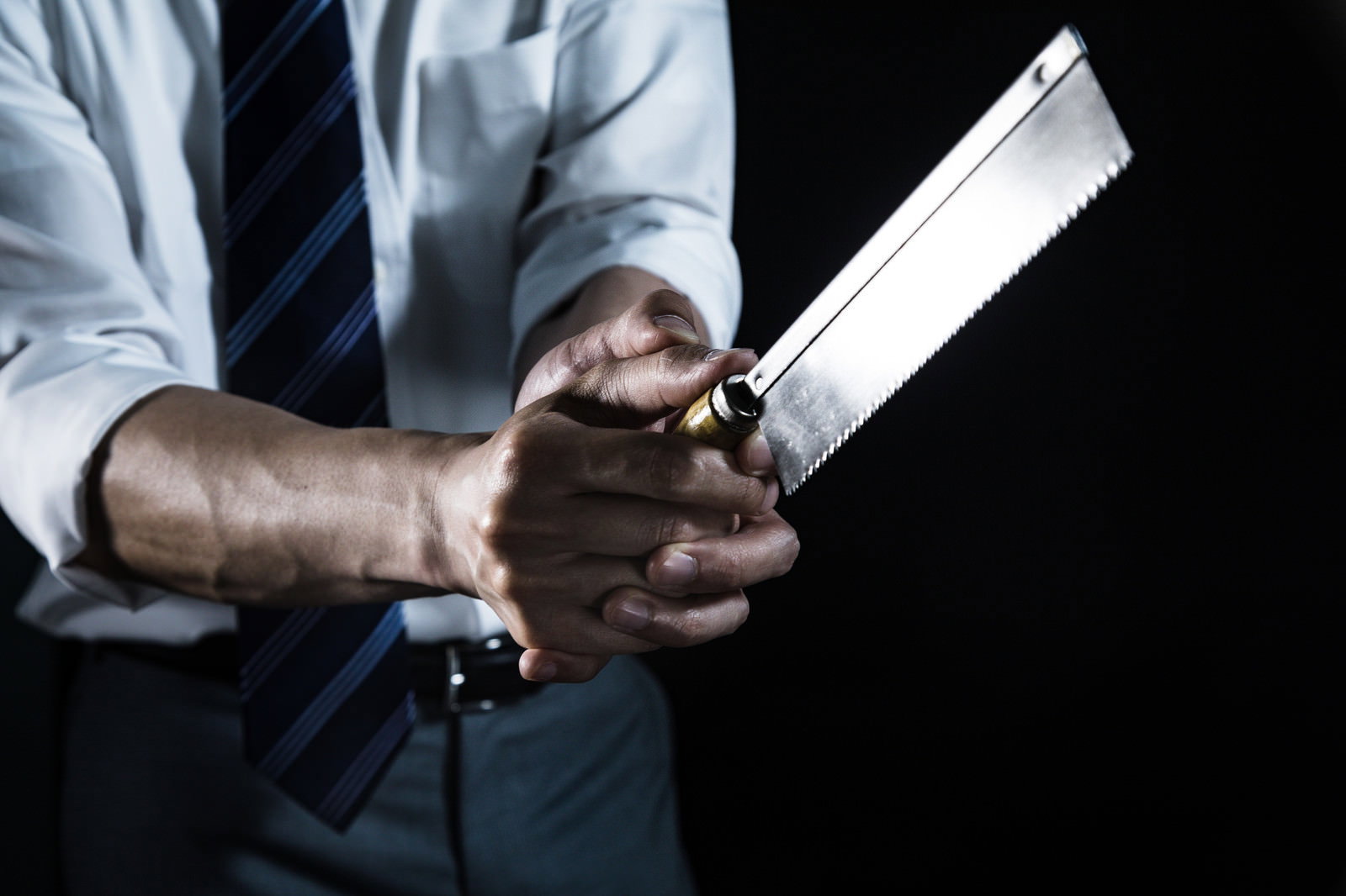 白いワイシャツと黒いネクタイを着た会社員がノコギリを両手で握っている［モデル：大川竜弥］