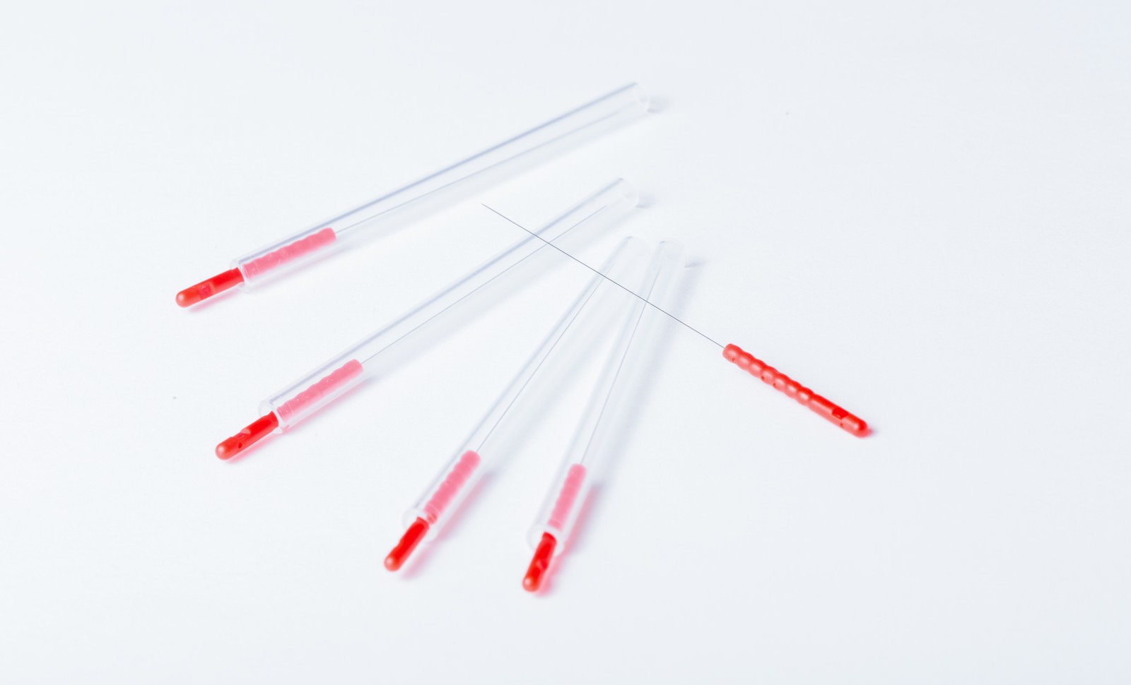 赤い鍼と透明な鍼管が白い背景に並べられている