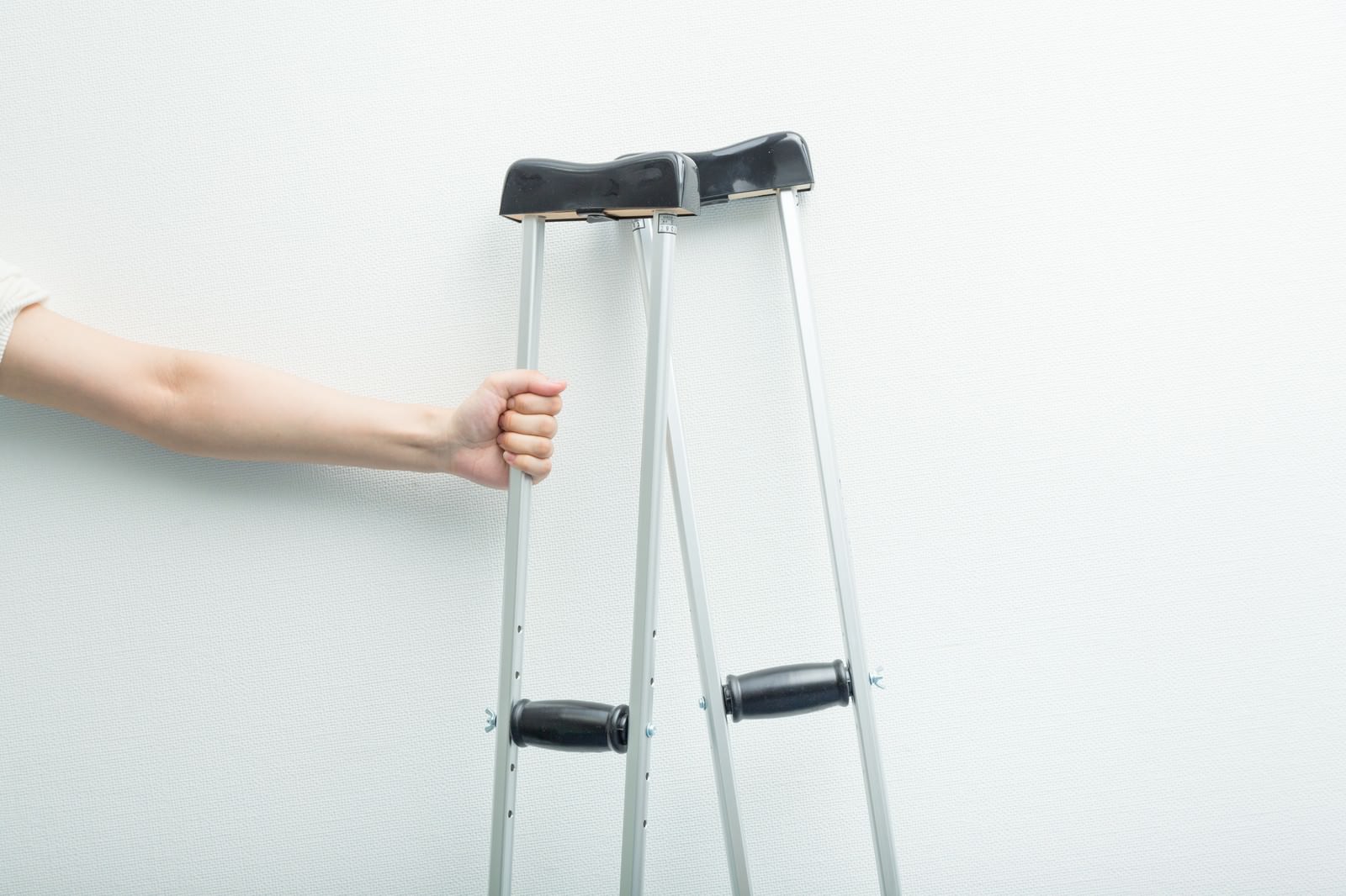 白いアルミ製の松葉杖を握りしめている男性の手