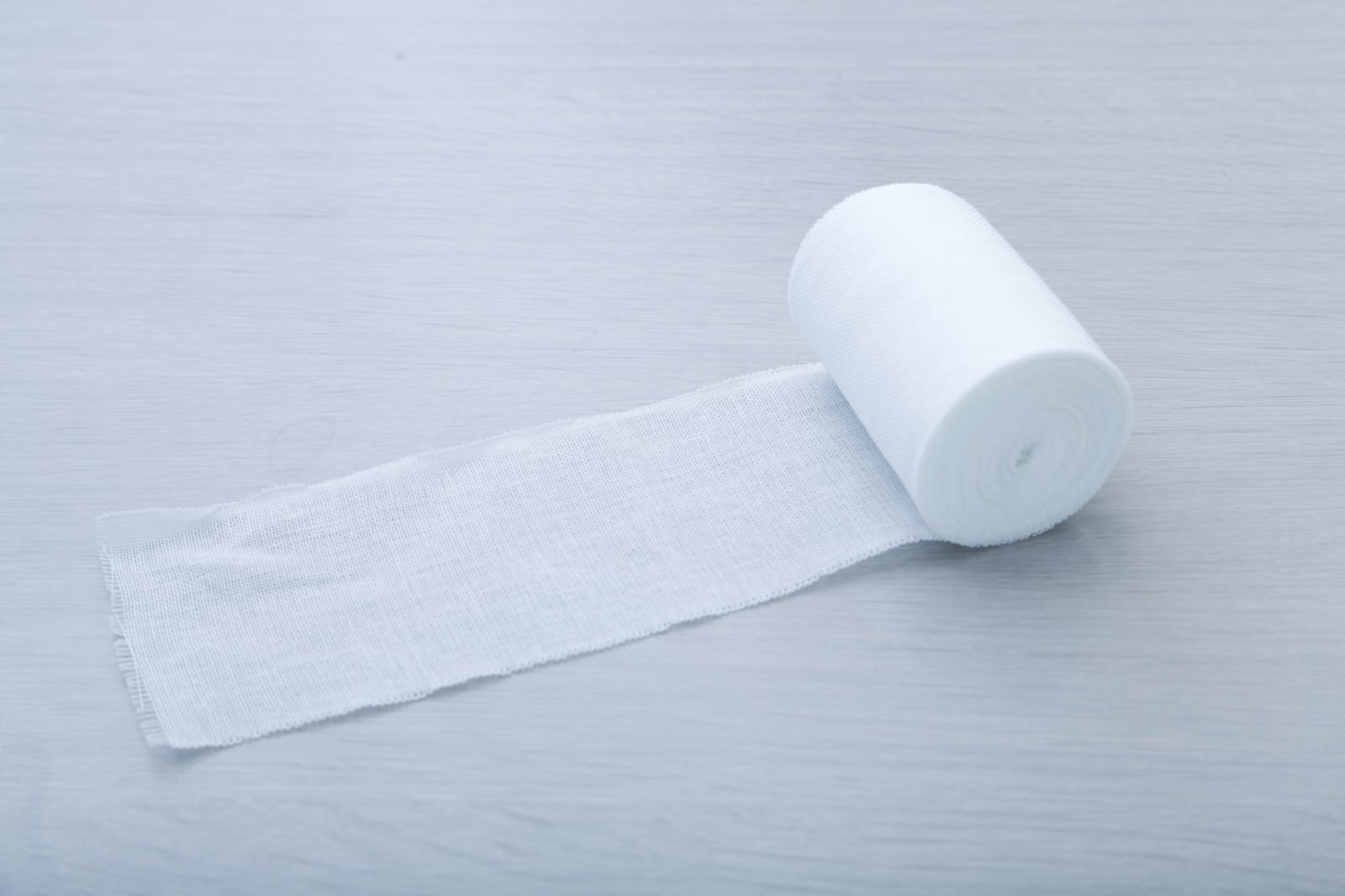 白い医療用包帯とガーゼロールが光の当たる白い布地の上に置かれている