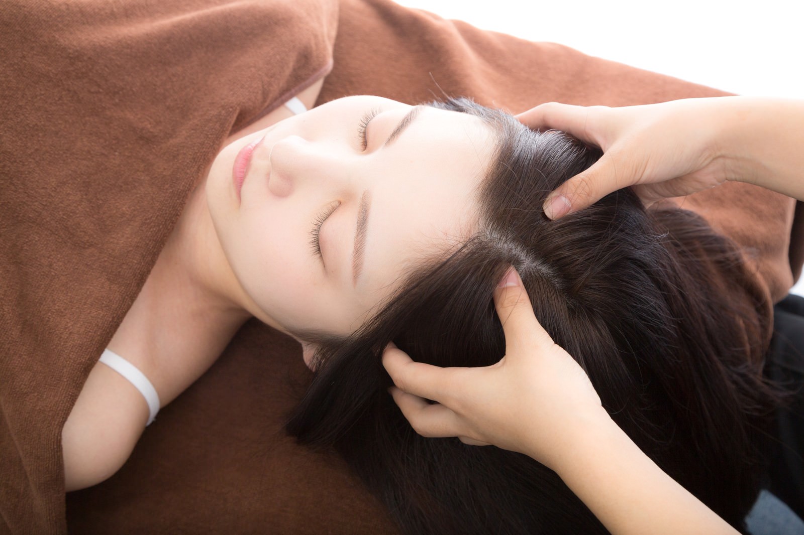 女性の頭のツボを指で押してマッサージする手もみ施術