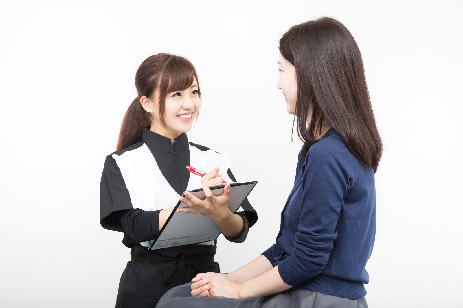 クリップボードを持ちながら患者に体調を問診する女性スタッフ［モデル：河村友歌］