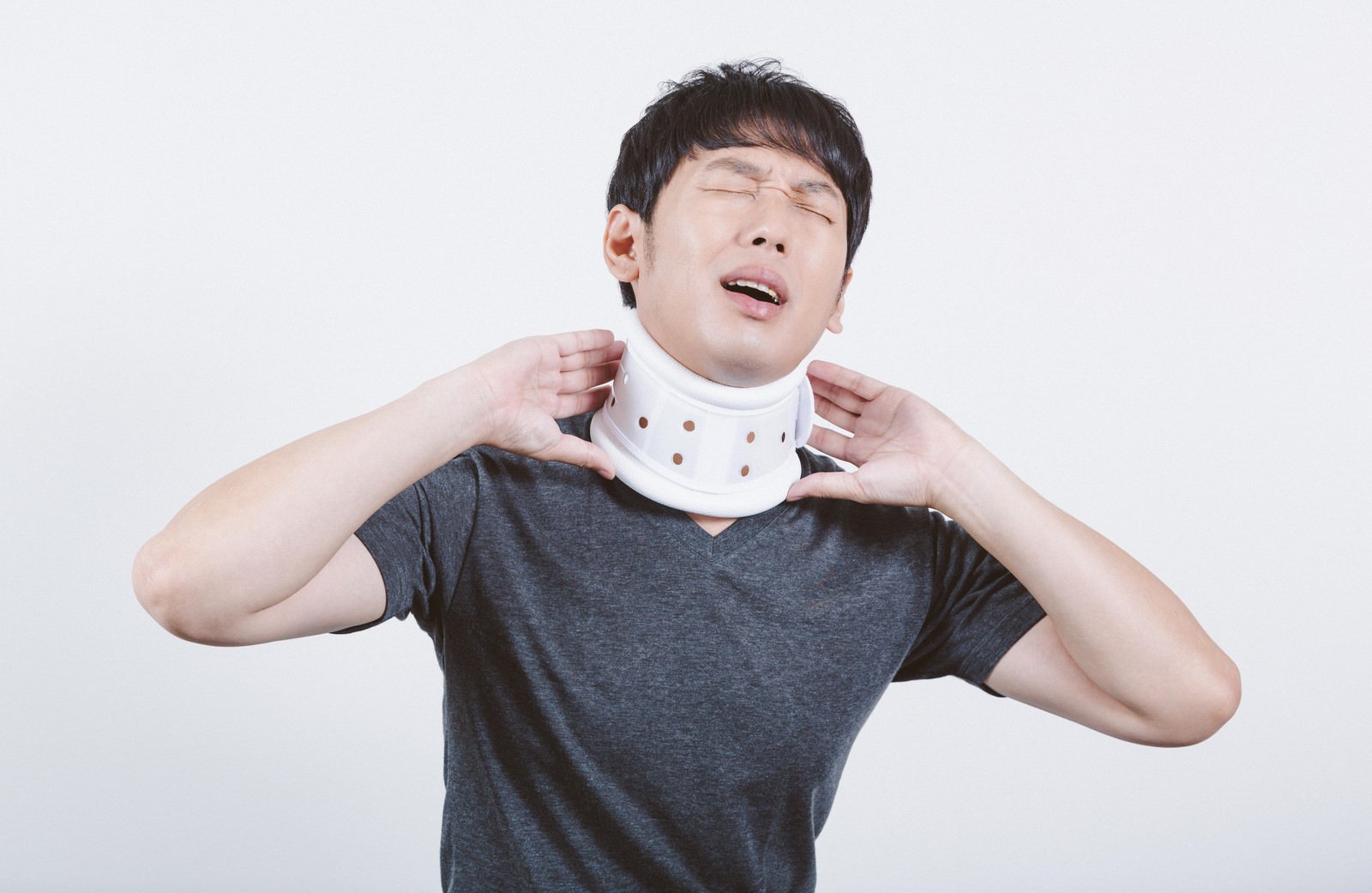 白い頚椎カラーを首に装着して痛みを感じる男性［モデル：大川竜弥］