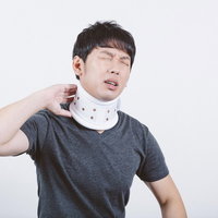 交通事故のむち打ちで首にコルセットを巻いて痛みに顔をしかめる男性の写真