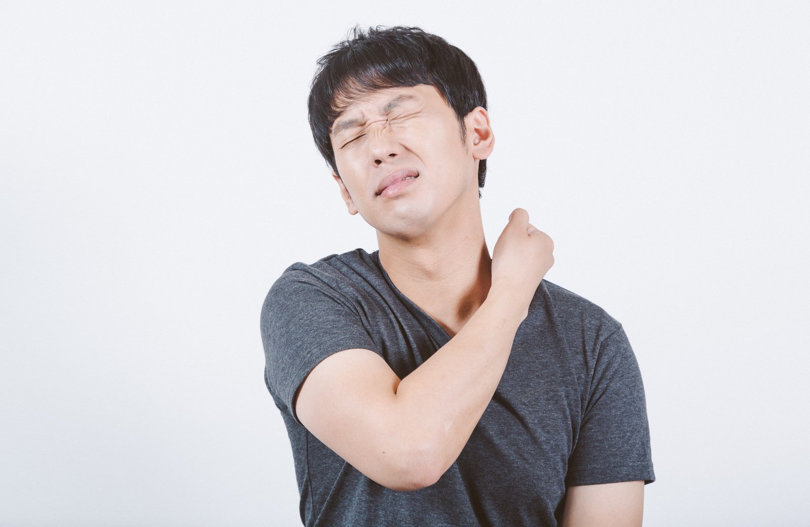首の痛みを感じて目をつむる男性が肩に手を当てている［モデル：大川竜弥］