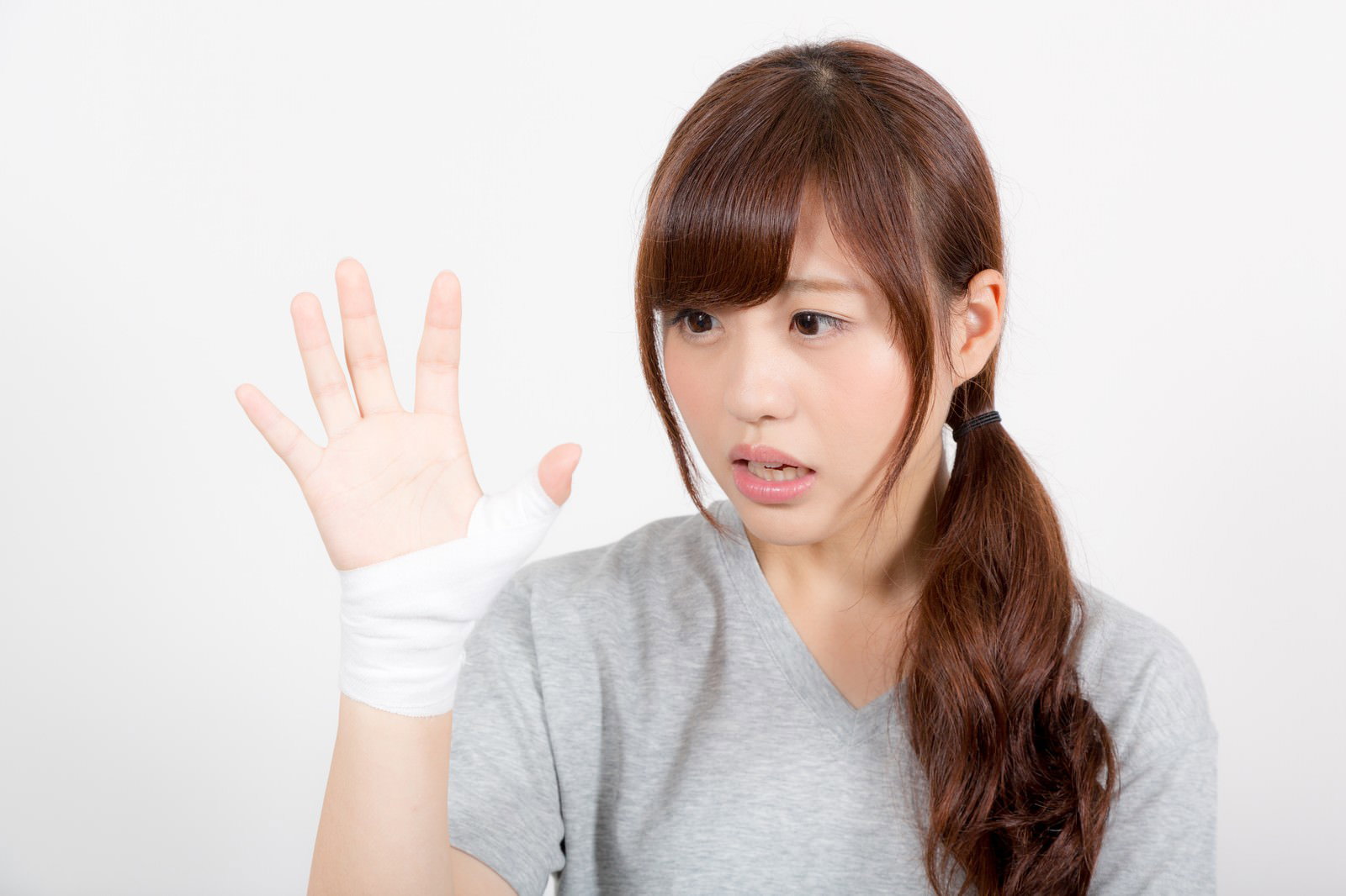 白いテーピングで親指を固定された女性が困った表情で横を向いている［モデル：河村友歌］