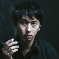 喫煙室で煙草を吸う男性の横顔、たばこの煙が漂う暗い空間の写真