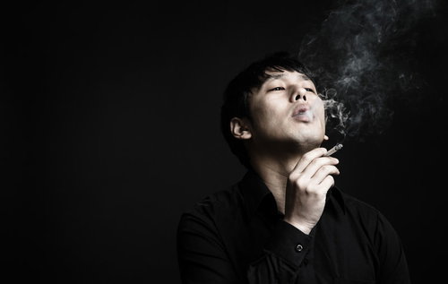 喫煙する眼鏡をかけた男性が口から煙を吐き出す