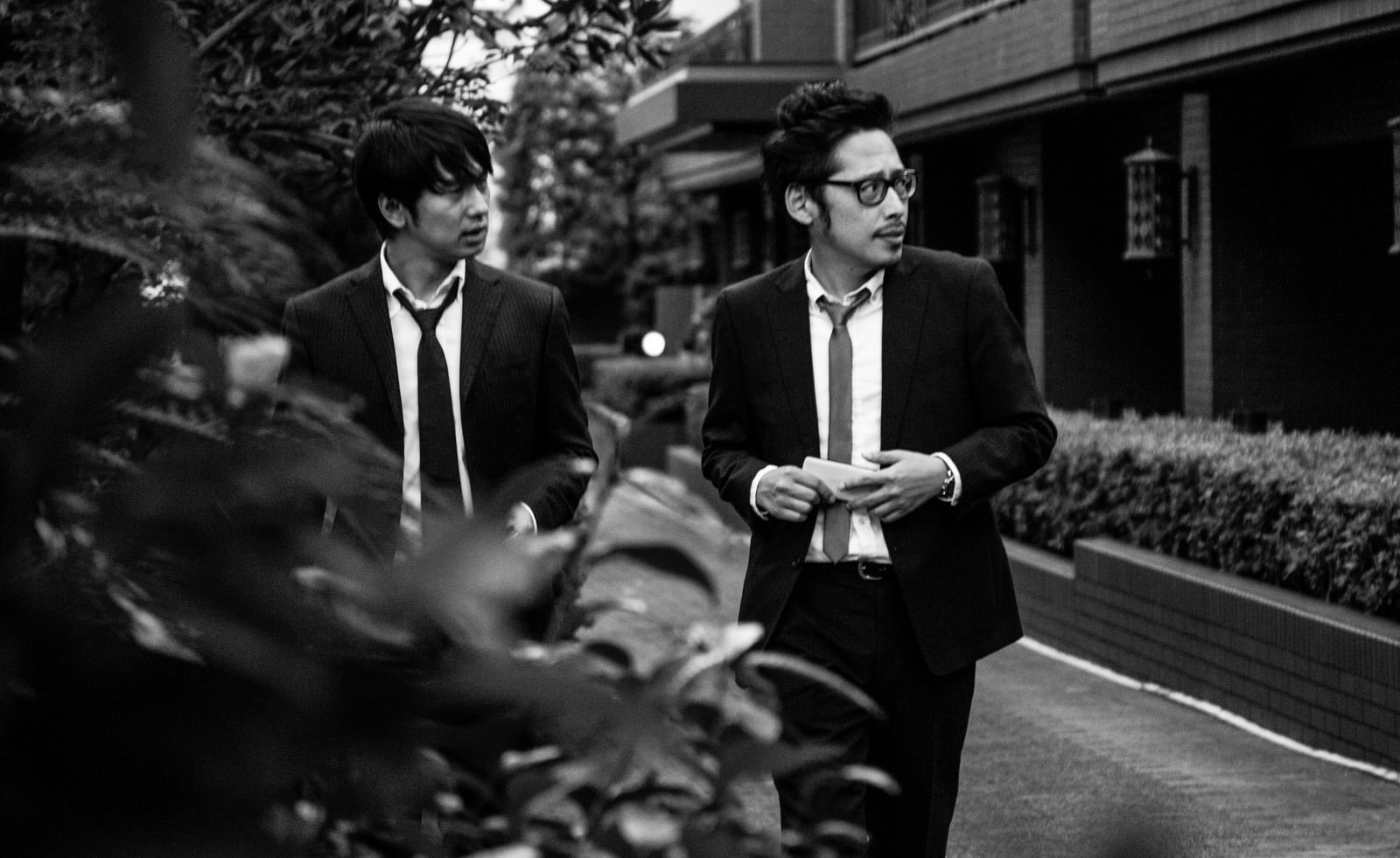 スーツ姿で街中を歩く二人の男性ジャーナリスト［モデル：大川竜弥 ゆうせい］