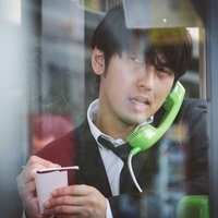 電話ボックスのピンクチラシが気になるブン屋、受話器片手に考えるの写真