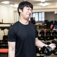 ダンベルを握りしめ歯を食いしばり自分を追い込むオールアウト厨の写真