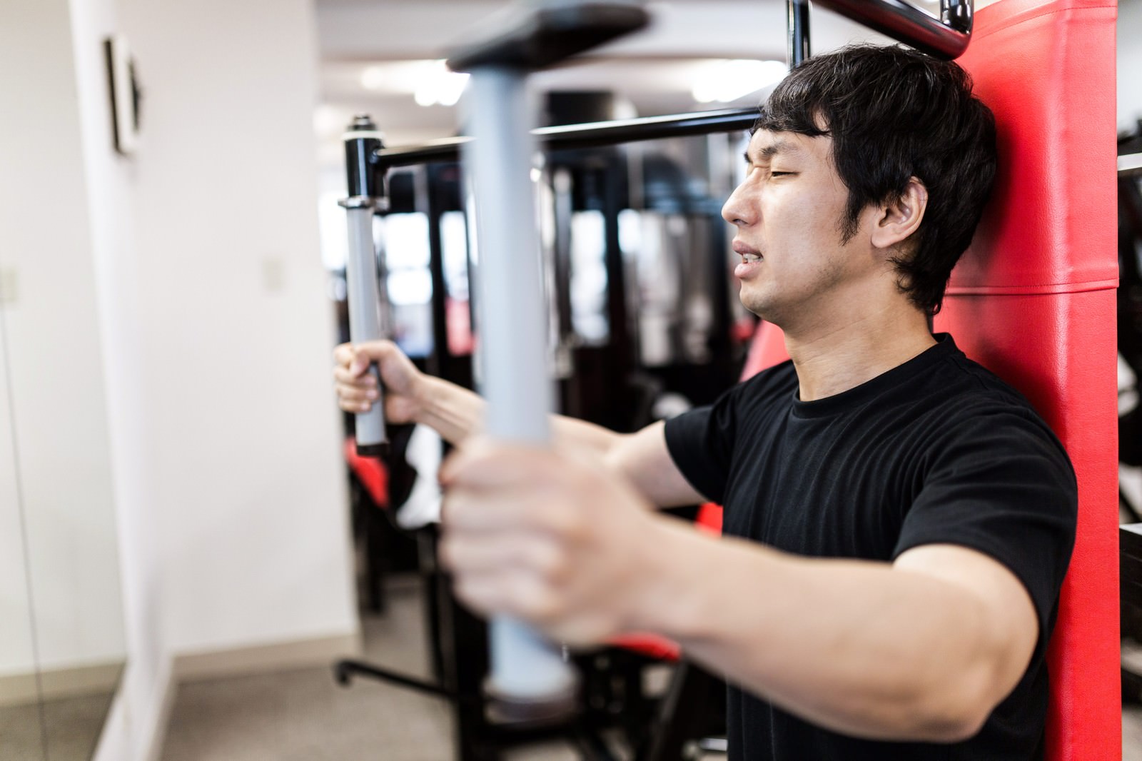 スポーツジムで胸部マシンを使用してトレーニングする男性［モデル：大川竜弥］