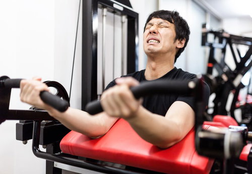 疲労物質が蓄積し限界を感じるトレーニー男性のダンベルエクササイズ