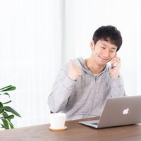 スマートフォンで通話しながらノートパソコンを操作する男性の写真