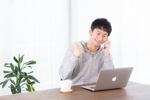 スマートフォンで通話しながらノートパソコンを操作する男性