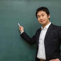 ニコニコしながらチョークを持つ先生の写真