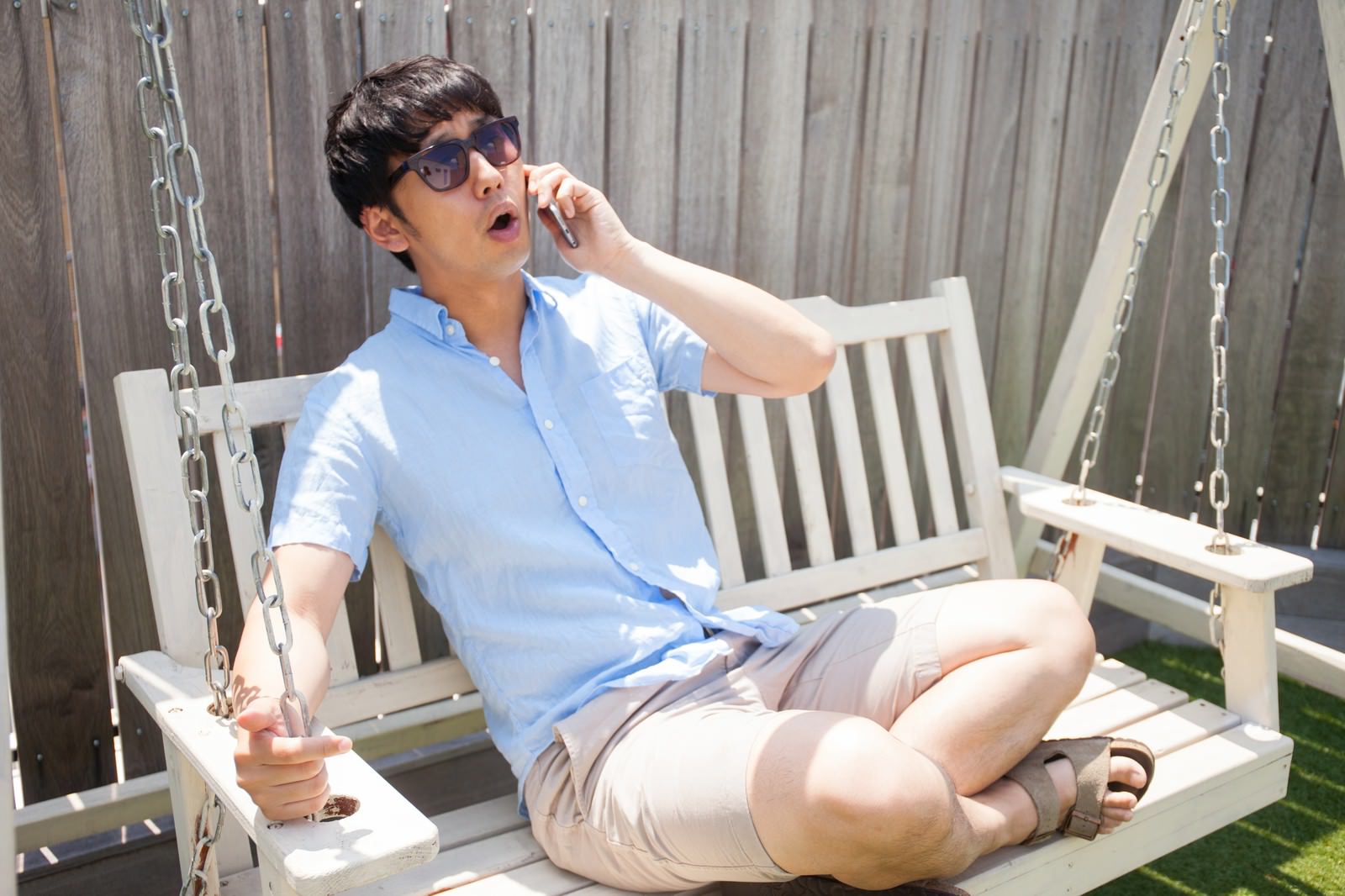 サングラスをかけてスウィングチェアで電話をする男性［モデル：大川竜弥］