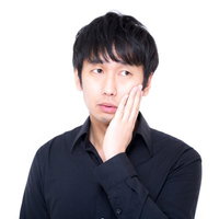 右手を頬に当てて視線を外す黒い長袖シャツの黒髪男性の写真