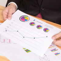 グラフ資料を両手で持って見せるスーツの男性の写真